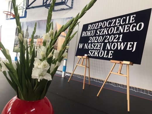 zdjęcie wazono z kwiatami obok, którego ustawiona jest tablica z napisem "ROZPOCZĘCIE ROKU SZKOLNEGO 2020/2021 W NASZEJ NOWEJ SZKOLE"