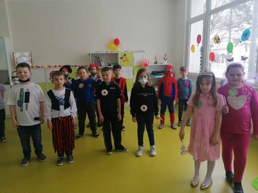 Uczniowie w swoich przebraniach karnawałowych stoją w sali lekcyjnej i usmiechają się do zdjęcia.