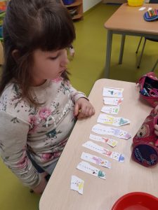 Przy stoliku siedzi uczennica przed którą leżą kawałki papieru z narysowanymi bałwankami.