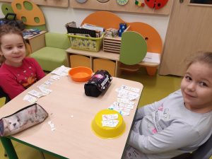 Przy stoliku siedzą dwie uczennice przed którymi leżą kawałki papieru z narysowanymi bałwankami.