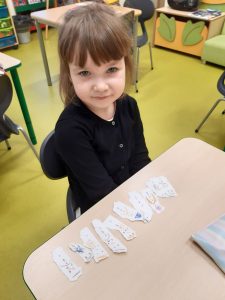 Przy stoliku siedzi uczennica przed którą leżą kawałki papieru z narysowanymi bałwankami.