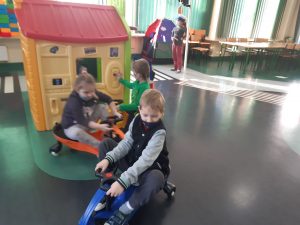 Zdjęcie wykonane na zajęciach w toruńskim WORDzie przedstawia dwoje dzieci jeżdżących na mini rowerkach przed domkiem dla dzieci do zabawy.