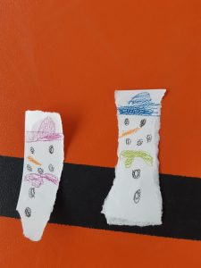 Na pomarańczowym tle umieszczono dwa kawałki papieru z narysowanymi bałwankami.