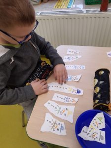 Chłopiec pochyla się nad stolikiem na którym leżą kawałki papieru z narysowanymi bałwankami.