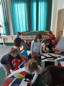 Zdjęcie wykonane na zajęciach w toruńskim WORDzie przedstawia dzieci układające kolorowe sześciany w znak drogowy.