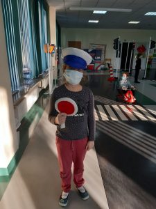 Zdjęcie wykonane na zajęciach w toruńskim WORDzie przedstawia uczennicę w czapce policjanta z lizakiem w dłoni. W tle widać sale edukacyjną z przejściem dla pieszych.