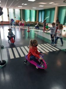 Zdjęcie wykonane na zajęciach w toruńskim WORDzie przedstawia dzieci jeżdżące po sali edukacyjnej na mini rowerkach.