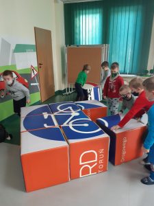 Zdjęcie wykonane na zajęciach w toruńskim WORDzie przedstawia uczniów układających znak drogowy z sześciennych kostek.