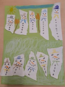 Na zielonej kartce papieru naklejono kawałki białej kartki z narysowanymi na nich bałwankami.