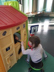 Zdjęcie wykonane na zajęciach w toruńskim WORDzie przedstawia uczennicę siedzącą na mini rowerku i zaglądającą do środka plastikowego domku.