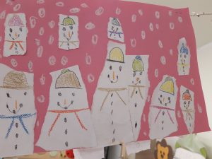 Na czerwonej kartce papieru naklejono narysowane przez uczniów bałwanki na paskach białego papieru.