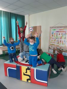 Zdjęcie wykonane na zajęciach w toruńskim WORDzie przedstawia uczniów klęczących z podniesionymi rękami na kolorowych kostkach w kształcie sześcianów.