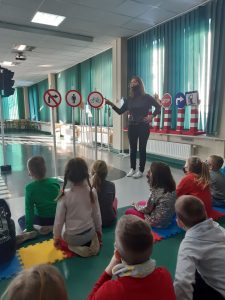 Zdjęcie wykonane na zajęciach w toruńskim WORDzie przedstawia Panią wskazującą na znaki drogowe i uczniów, którzy siedząc na podłodze ją słuchają.