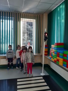 Zdjęcie wykonane na zajęciach w toruńskim WORDzie przedstawia uczniów ustawionych w rzędzie i czekających na przejściu dla pieszych na zielone światło.