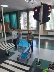 Zdjęcie wykonane na zajęciach w toruńskim WORDzie przedstawia uczennicę trzymającą dziecięcy wózek i czekających na zielone światło przed przejściem dla pieszych.