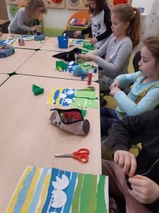 Przy stole siedzą uczniowie, którzy kończą swoje prace plastyczne z przebiśniegami.