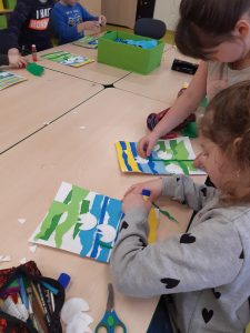 Przy dużym stole siedzą uczniowie wykonujący prace plastyczne z kawałków kolorowego papieru.