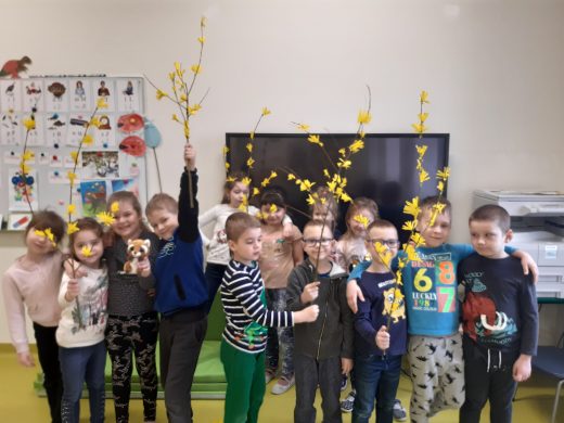 Na zdjęciu widoczni są wszyscy uczniowie trzymający w dłoniach zrobione przez siebie gałązki z żółtymi kwiatkami.