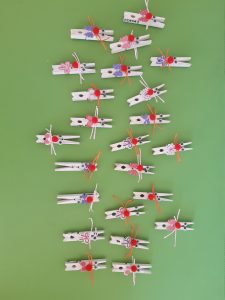 Na zielonym tle umieszczono 23 białe klamerki przybrane kokardkami i czerwonymi pomponami w miejscu nosa tak by wyglądały jak króliczki.