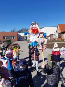 Zdjęcie uczniów wychodzących ze szkoły i trzymających w rękach wykonane przez siebie marzanny.