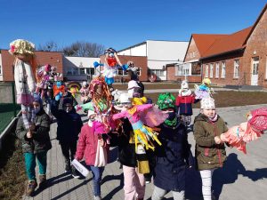 Zdjęcie uczniów wychodzących ze szkoły i niosących wykonane przez siebie marzanne.