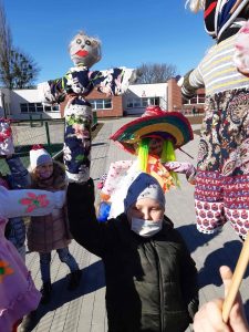 Zdjęcie uczniów stojących przed szkołą i trzymających w rękach marzanny.