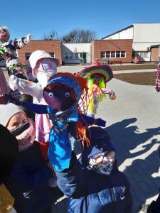 Zdjęcie uczniów stojących przed szkołą i trzymających wykonane przez siebie marzanny.