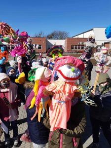 Zdjęcie uczniów trzymających wykonane przez siebie kukiełki, stojących przed szkołą.