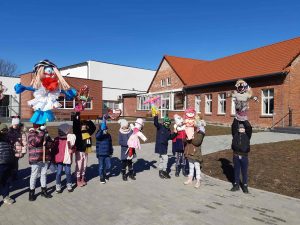 Zdjęcie uczniów stojących przed szkołą i trzymających wykonane przez siebie marzanny.
