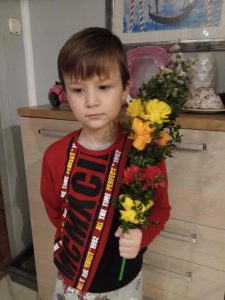 Uczeń stoi przed komodą i trzyma w lewej dłoni swoją palmę wielkanocną.