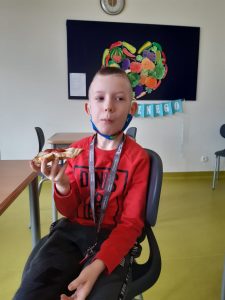 Na zdjęciu uczeń siedzi na krześle. W prawej dłoni trzyma tosta.