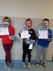 Na tle ściany stoi troje uczniów trzymających w lewych dłoniach dyplomy.