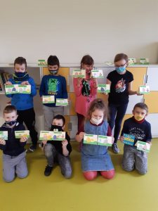 Uczniowie klasy drugiej ustawieni w dwóch rzędach. Każdy z nich trzyma w dłoniach po dwie wykonane odręcznie kartki świąteczne.