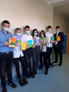 Uczniowie klasy ósmej stoją pod ścianą w rzędzie i trzymają w dłoniach wykonane przez siebie kartki.