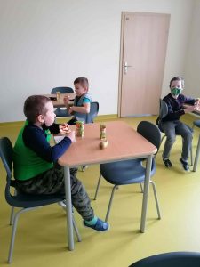 Zdęcie sali lekcyjnej. Trzech uczniów siedzi przy stolikach jednoosobowych rozstawionych na sali.