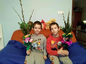 Dwóch uczniów siedzi na kanapie. Każdy z nich trzyma wykonaną przez siebie palmę wielkanocną.