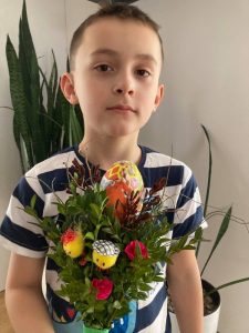 Uczeń a przed nim wiązanka z bukszpanu udekorowana pisanką i sztucznymi kurczaczkami.