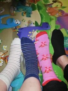 Na wielokolorowym tle w dinozaury widoczne są cztery stopy ubrane w skarpetki różnego koloru i w różne wzory.