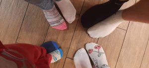Na drewnianej podłodze widoczne są stopy czterech osób stojących w kółu. Każda stopa ubrana jest w inną skarpetkę.