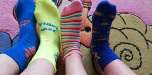 Dywan w kolorach pastelowych na tle którego widoczne są cztery stopy w różnokolorowych skarpetkach.