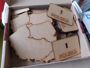 Karton w którym umieszczono elementy modelu mapy Polski - podstawki z napisem POLSKA oraz wyciete ze sklejki mapy naszego kraju.