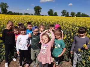 Grupka dzieci stoi na tle pola zasianego rzepakiem.
