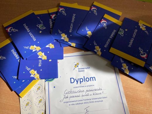 Zdjęcie Dyplomu uczestnictwa w projekcie "Ciekawskie pierwszaki. Jak poznać świat w klasie ?". Nad dyplomem rozłożone są w półkolu niebieskie karteczki z rysunkami rakiet kosmicznych i napisem "Indeks ucznia".