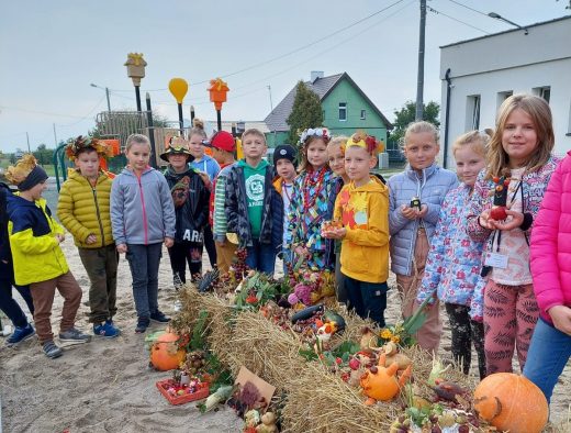 Uczniowie klasy trzeciej pozują do zdjęcia ustawieni w okół belek siana, na jtórych zostały poukładane naturalne dary jesieni.