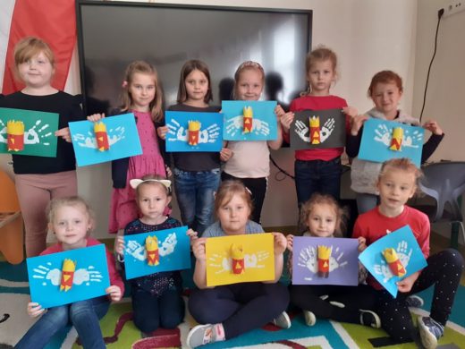 Dzieci z oddziału przedszkolnego pozują do zdjęcia ustawione w dwóch rzędach i trzymają w dłoniach swoje prace przedstawiąjące orły.
