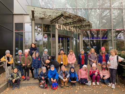 Uczniowie klasy pierwszej wraz z wychowawczynią pozują do zdjęcia przed wejściem do kina. Za nimi widać przeszklony budynek z napisem CINEMA CITY.