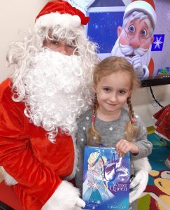 Uczennica oddziału przedszkolnego pozuje do zdjęcia z otrzymaną torebką z prezentami oraz Mikołajem.