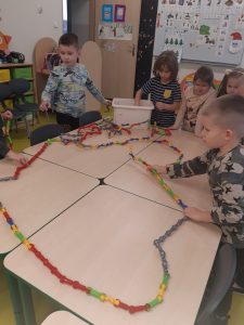 Uczniowie układają na stoliku łańcuch, który posłuży do stworzenia warstw w piramidzie żywienia.