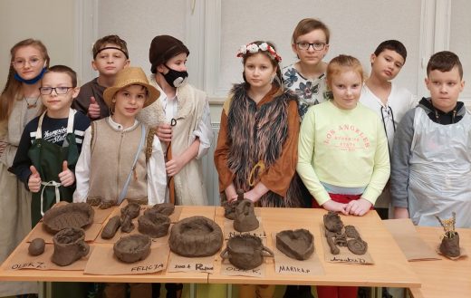 Uczniowie klasy trzeciej stoją w rzędzie w strojach słrojach słowiańskich za stołem, na którym ustawiono miski wykonane z gliny.