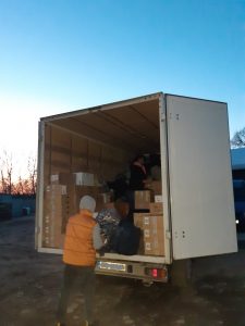 Zdjęcie tyłu ciężarówki z otwartymi drzwiami, do której mężczyzna stojący plecami pakuje torby. Samochów wypełniony jest kartonami i torbami.